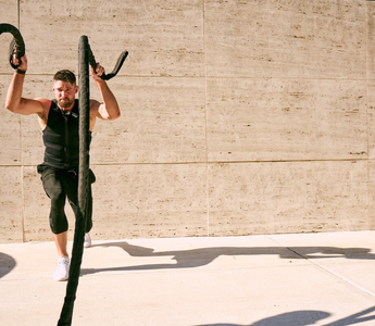 Fit man wearing a black Aion weighted vest performing battle rope training outdoors, showcasing strength, endurance, and functional performance