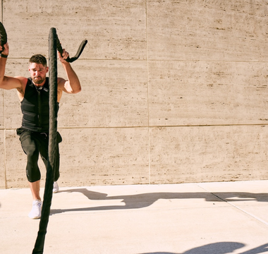 Fit man wearing a black Aion weighted vest performing battle rope training outdoors, showcasing strength, endurance, and functional performance