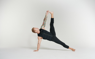 Man wearing an Aion weighted vest performing a side plank with a leg raise and overhead stretch. This functional fitness exercise builds core strength, balance, mobility, flexibility, and stability while adding resistance for greater muscle activation.