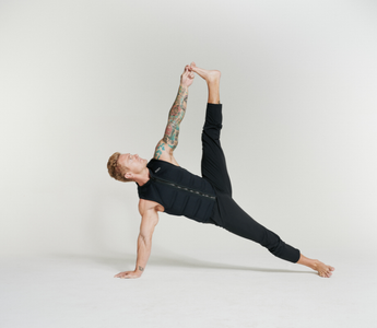Man wearing an Aion weighted vest performing a side plank with a leg raise and overhead stretch. This functional fitness exercise builds core strength, balance, mobility, flexibility, and stability while adding resistance for greater muscle activation.