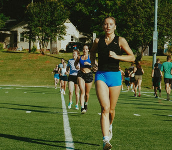 group fitness class on an outdoor sports field with a fit young woman running while wearing an Aion women's weighted vest