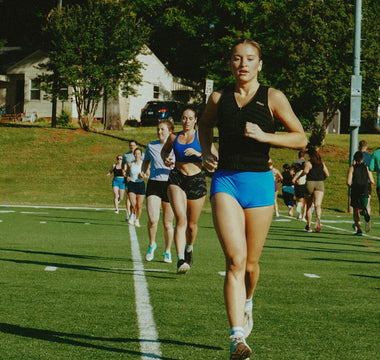 group fitness class on an outdoor sports field with a fit young woman running while wearing an Aion women's weighted vest