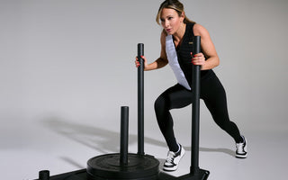 Aion Ambassador and world-renowned fitness cover model Paige Hathaway wearing an Aion weighted vest pushing a weighted sled