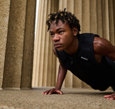 Athlete wearing a black Aion weighted vest performing push-ups outdoors between stone columns