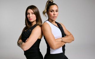 Two women stand back-to-back in Aion weighted vests with arms crossed, showcasing strength, confidence, and functional fitness.