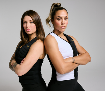 Two women stand back-to-back in Aion weighted vests with arms crossed, showcasing strength, confidence, and functional fitness.