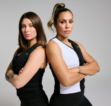 Two women stand back-to-back in Aion weighted vests with arms crossed, showcasing strength, confidence, and functional fitness.