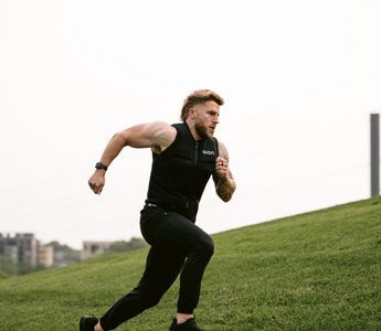 Athletic man sprinting uphill wearing an Aion weighted vest, showcasing high-intensity outdoor training for fat loss, endurance, and strength building.