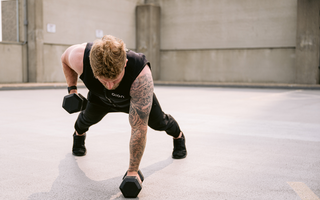 A fit man wearing a black Aion weighted vest performing a single-arm dumbbell row in a plank position outdoors, showcasing core stability, strength training, and functional fitness performance.