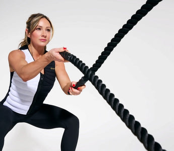 Paige Hathaway World-renowned fitness cover model, entrepreneur, and fitness influencer wearing the Aion women's weighted vest while in a squat position throwing ropes