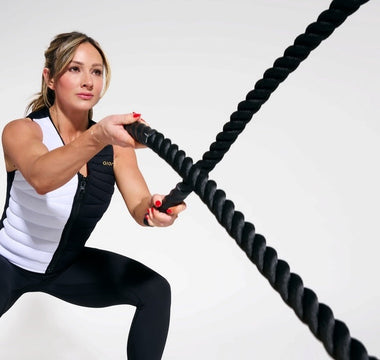 Paige Hathaway World-renowned fitness cover model, entrepreneur, and fitness influencer wearing the Aion women's weighted vest while in a squat position throwing ropes