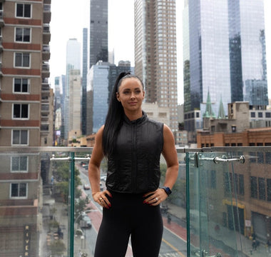 a fit young woman wearing the Aion Women's Weighted Walking Vest at Life Time Fitness Club NYC outdoor patio with NYC skyline in the background